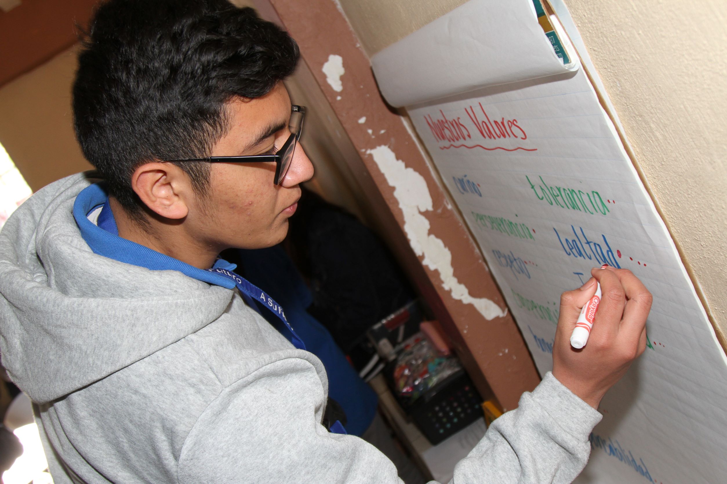 A male student writes on a poster titles "Our Values" in Spanish.